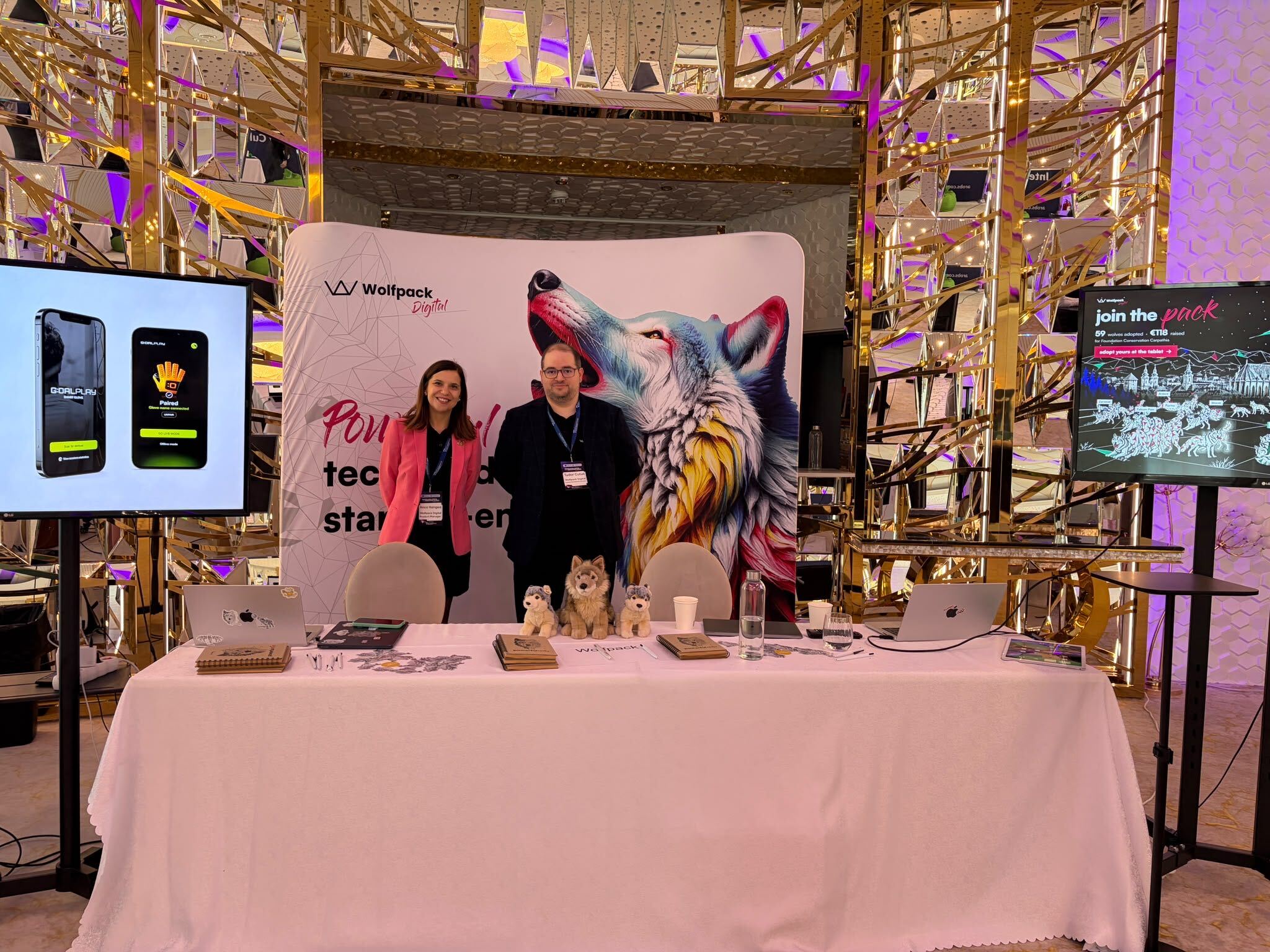 ee6e8379 b020 49cb a871 Anca Hangea and Tudor Cutus at the Wolfpack Digital booth at Transilvania Digital Innovation Summit 2026, with a howling wolf backdrop, plush wolves on the table and the Join the Pack screen on the right.