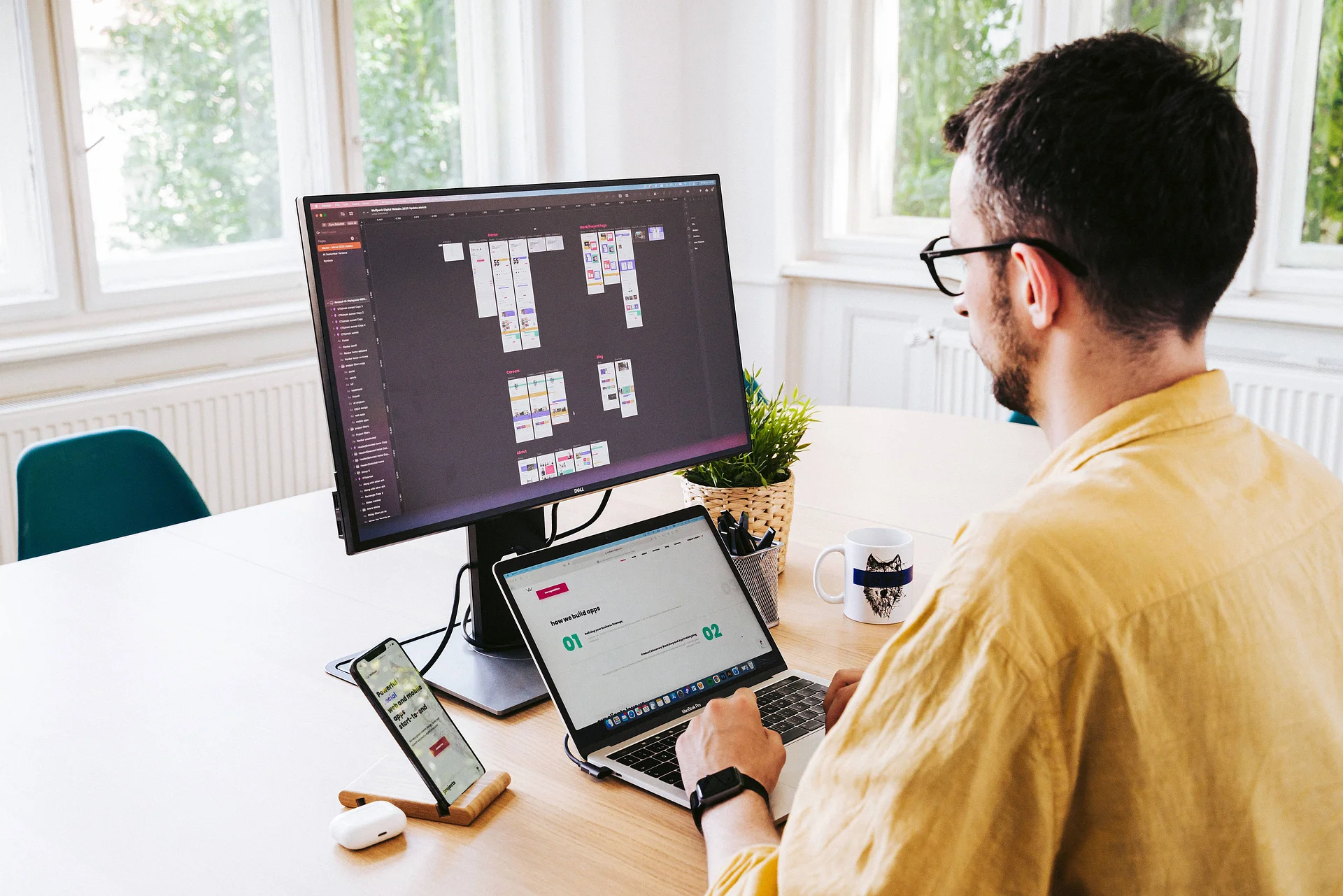 Photo of a developer working at a desk with code displayed on a monitor, a laptop, and a smartphone, representing software development and multi-device workflows."