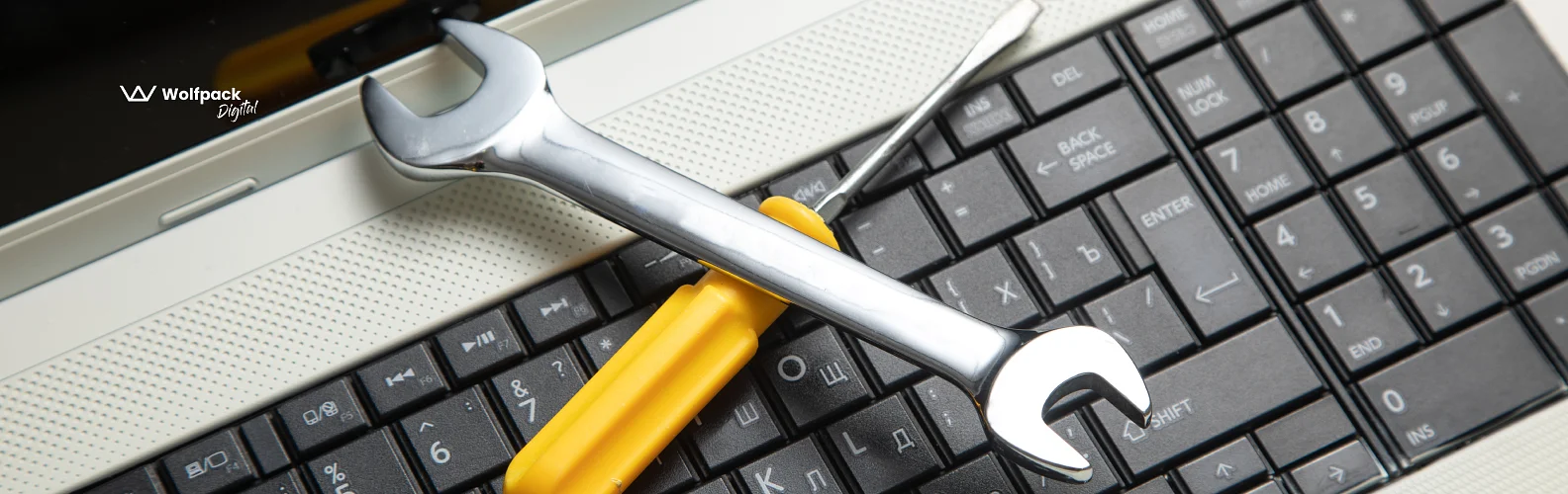 Wrench and screwdriver resting on a laptop keyboard, illustrating QA testing for hardware-connected apps