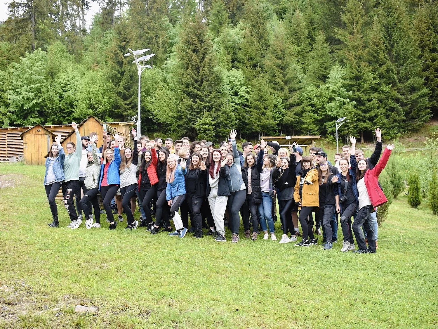 The full Wolfpack Digital team cheering outdoors by wooden cabins during their School Trip in the Apuseni Mountains