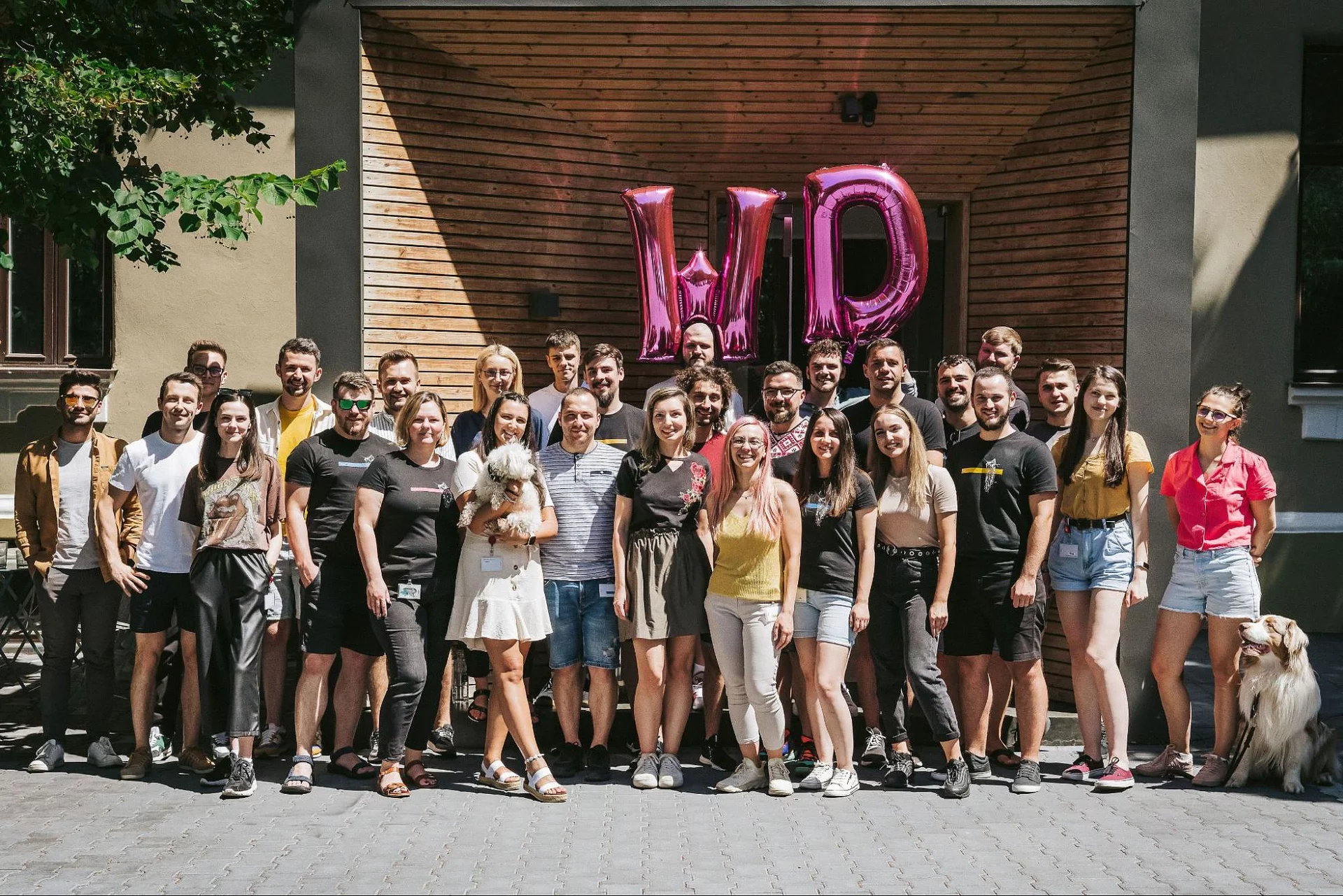 The full Wolfpack Digital team posing outdoors in front of large pink WD foil balloons in summer 2022