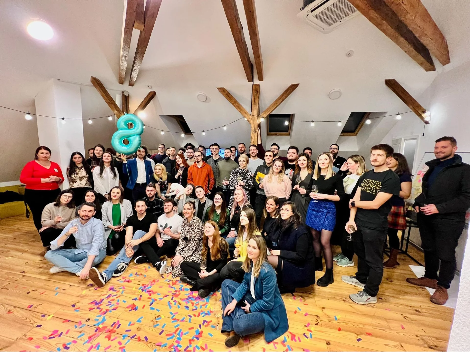The full Wolfpack Digital team gathered at the office holding a large teal number 8 balloon for the company's 8th anniversary