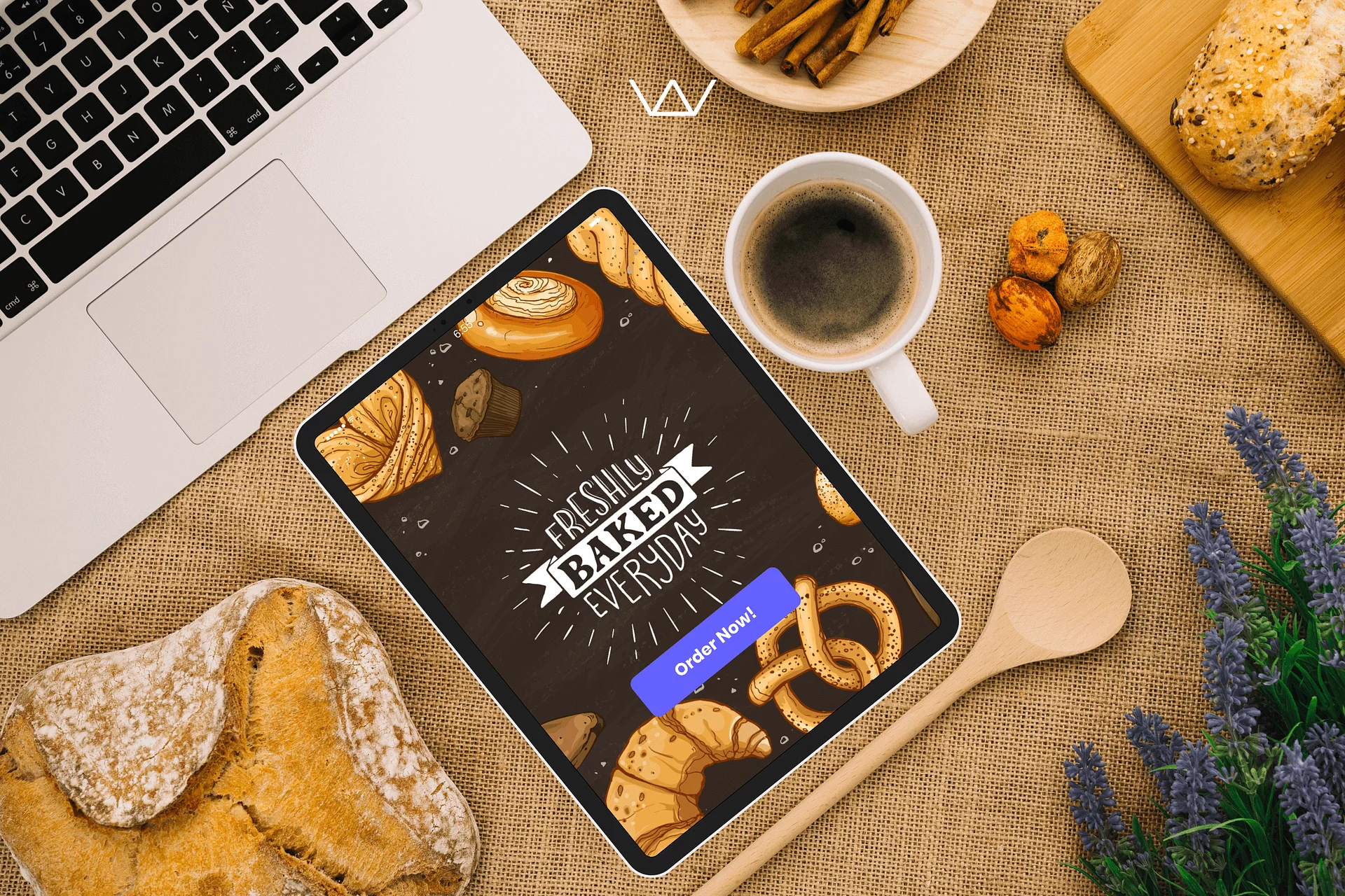 A tablet showing a bakery app that reads 'Freshly Baked Everyday' with an Order Now button, beside a laptop and coffee.