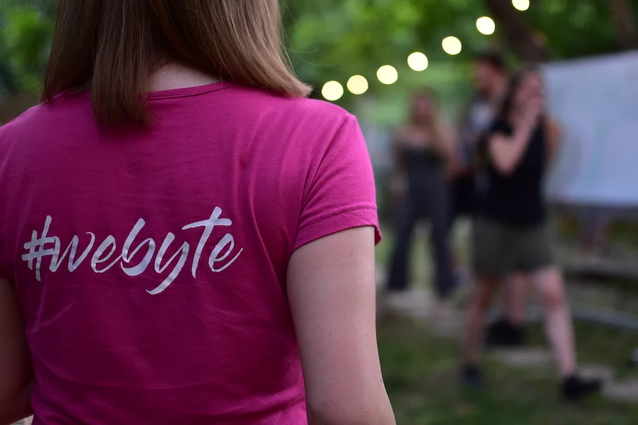 A Wolfpack Digital team member wearing a pink #webyte t-shirt, with colleagues in the background